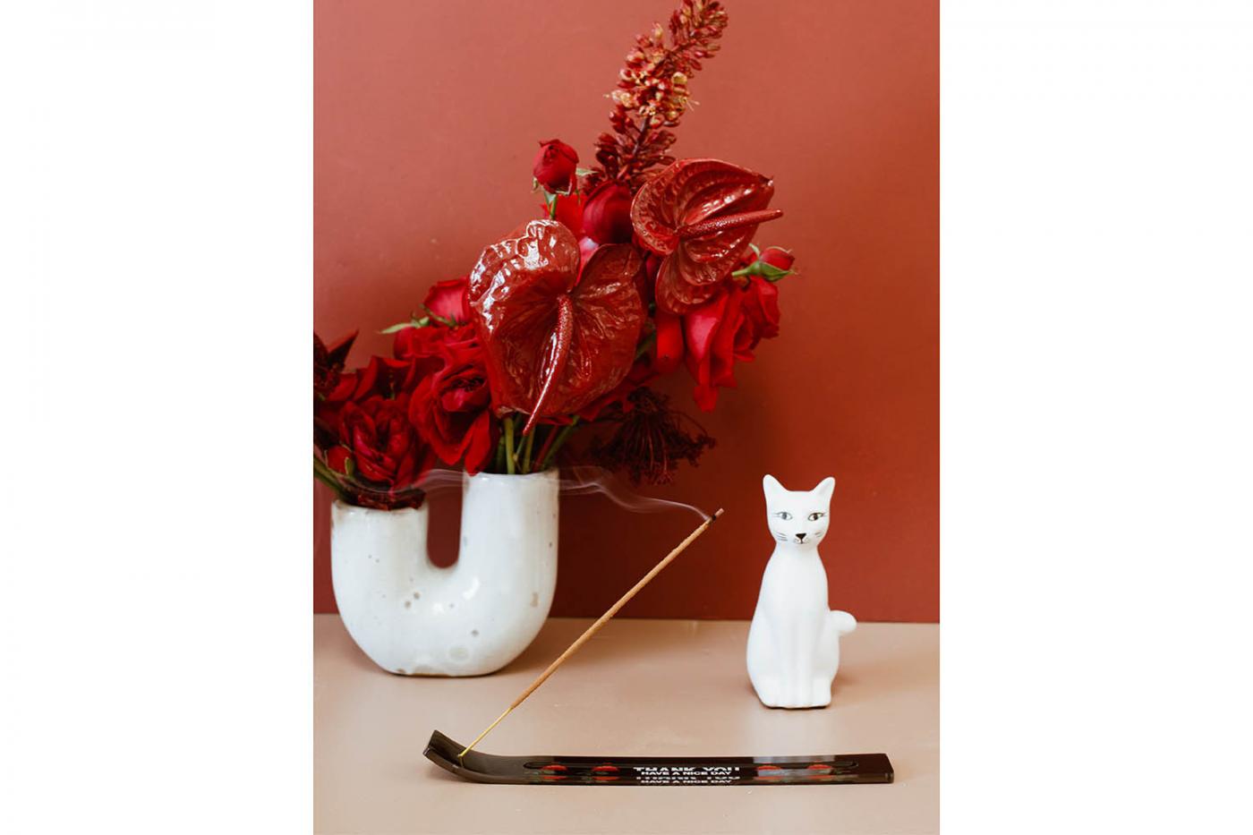 incense burning, cat statue and red florals sitting on table